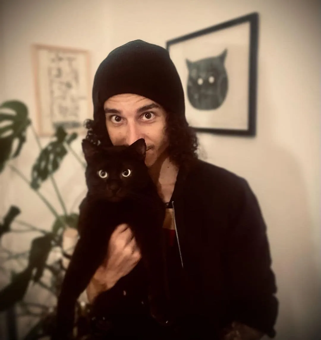 Matthew Seccafien and his black cat Otto standing in his Berlin apartment.